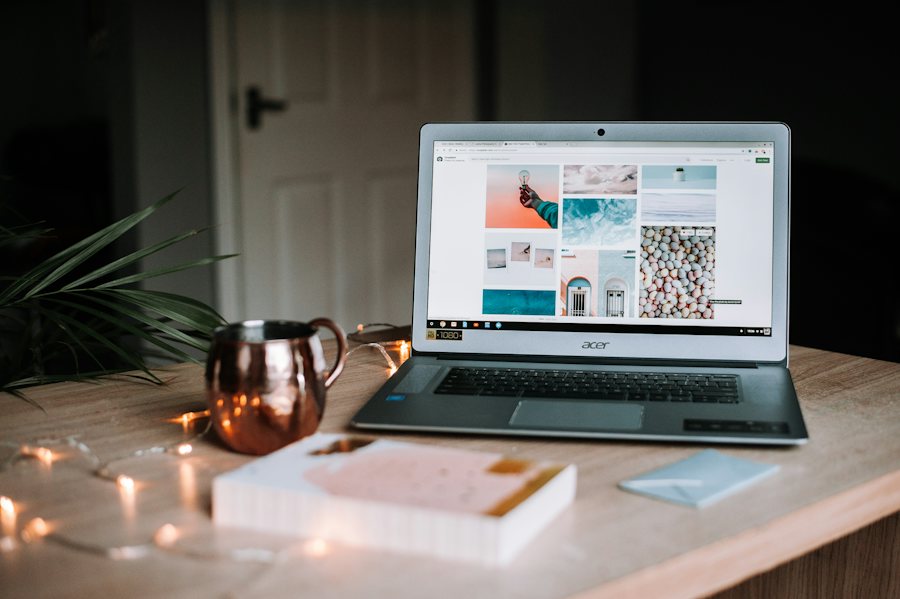 A laptop on a desk beside a copper mug and a notebook